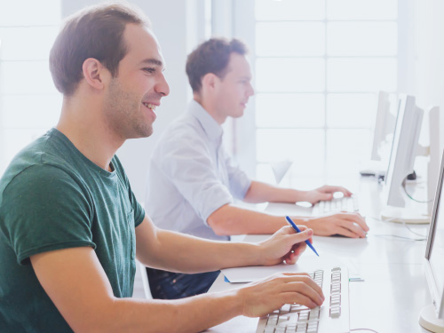 Two men in front of their computers attending a classroom course 