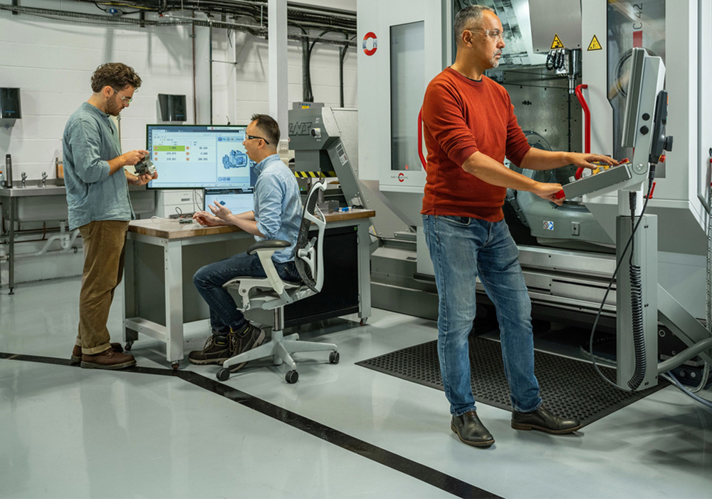 3 hombres situados en un entorno de mecanizado avanzado con equipos de precisión, mostrando innovación en los flujos de trabajo de fabricación